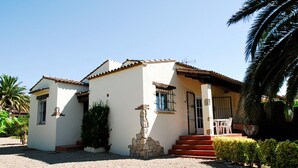 Une maison à deux étages, à l’extérieur blanc, avec une statue en pierre devant et un petit patio comprenant une table et des chaises.