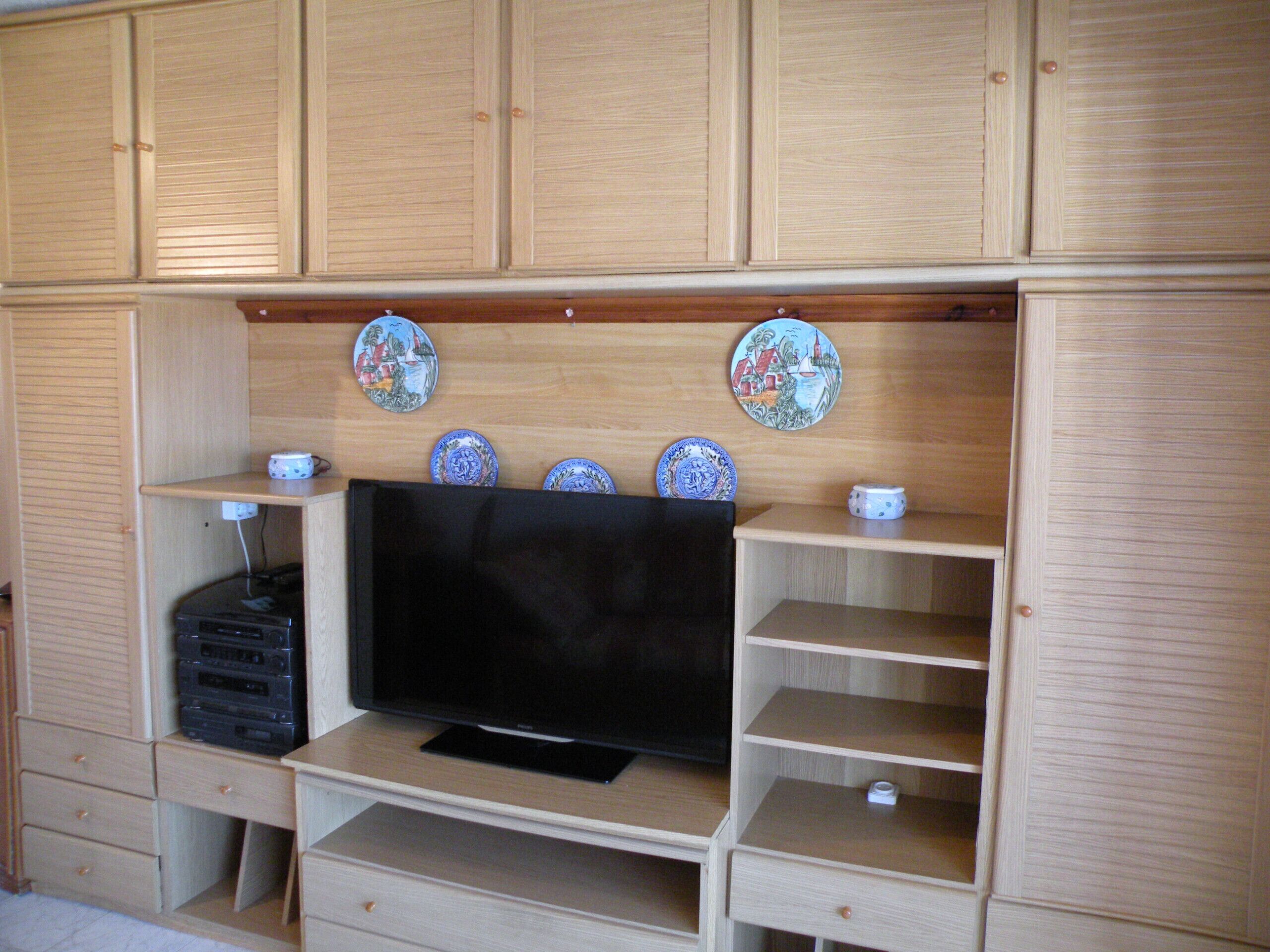 Uma unidade de entretenimento de madeira com uma TV de tela plana, gavetas e pratos decorativos.