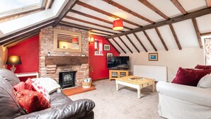 A cozy loft-style living room with a fireplace, a television, and a high ceiling with exposed beams.