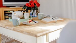 A breakfast setup with a plate of food, a book, glasses, and a vase of flowers on a wooden table.