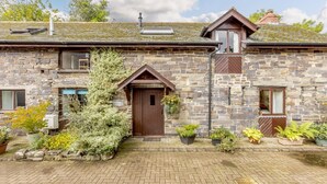 A stone cottage with a central wooden door, a small porch, and potted plants.