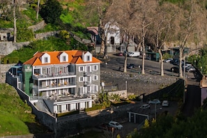 A multi-story hotel with balconies, a parking area, and a stone wall. - 1-bed Loft Superior Suite in Babosas Village (Funchal)