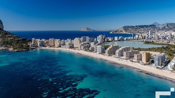 Paisagem costeira com praia, edifícios altos e águas azuis cristalinas.