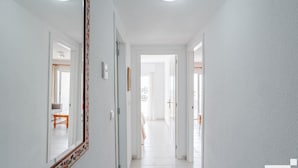 Corredor com paredes brancas, piso de madeira e espelho com detalhes florais.