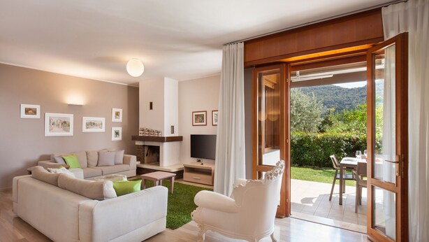 Un salon moderne avec un canapé, un fauteuil et un téléviseur. Une porte-fenêtre coulissante donne accès à un espace extérieur aménagé avec une table et des chaises.