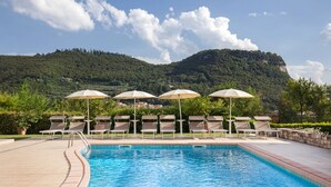 Un espace piscine doté de chaises longues et de parasols, entouré de verdure et avec une chaîne de montagnes en toile de fond.