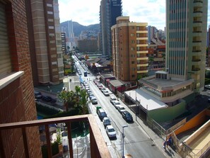 Una calle urbana con edificios altos, una vía transitada y una montaña al fondo.
