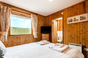 Habitación con paneles de madera, una cama, un televisor y un ventanal con cortinas.