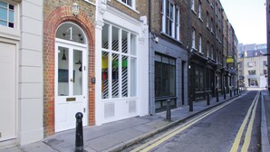 Une vue de rue avec une rangée de bâtiments, dont un magasin avec une porte blanche et un banc à l’extérieur.