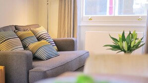 Un salon avec un canapé gris, des coussins à motifs, une lampe sur pied et une plante en pot.
