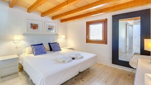Een slaapkamer met een houten plafond, een bed met witte lakens, twee wandlampen en een grote spiegel.
