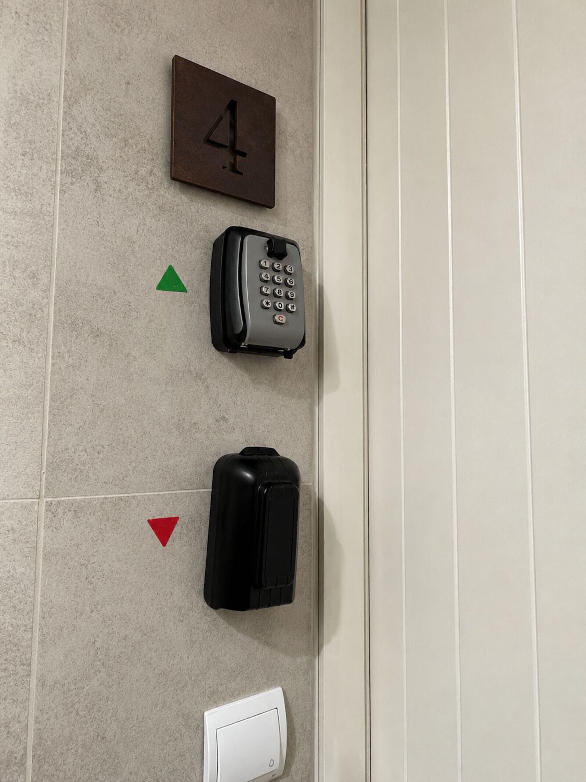 Un téléphone fixé au mur, une plaque indiquant le numéro de la chambre, une valise noire et un interphone blanc.