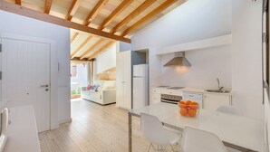 Een moderne keuken met witte kasten, een roestvrijstalen spoelbak en een ingebouwde oven. Er is een eethoek met een witte tafel en stoelen.
