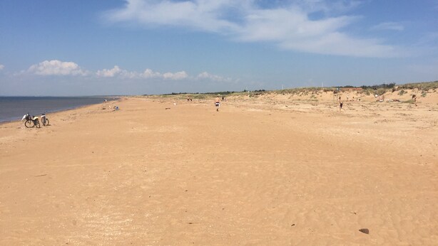 Een uitgestrekt zandstrand met een heldere lucht en enkele mensen in de verte.