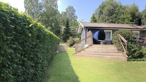 Een verzorgde tuin met een houten terras dat leidt naar een huis met een pannendak.