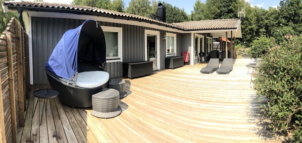 A covered outdoor area with a wooden deck, a covered seating area with a table and chairs, and a barbecue grill.