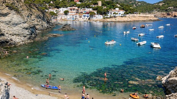 A coastal town with clear waters, boats, and people on the beach.
