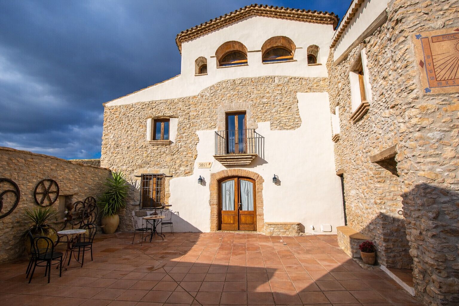 Un edificio de piedra con un patio empedrado, una puerta de madera y un balcón.