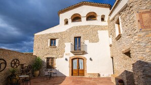 A stone building with a tiled patio, a wooden door, and a balcony.