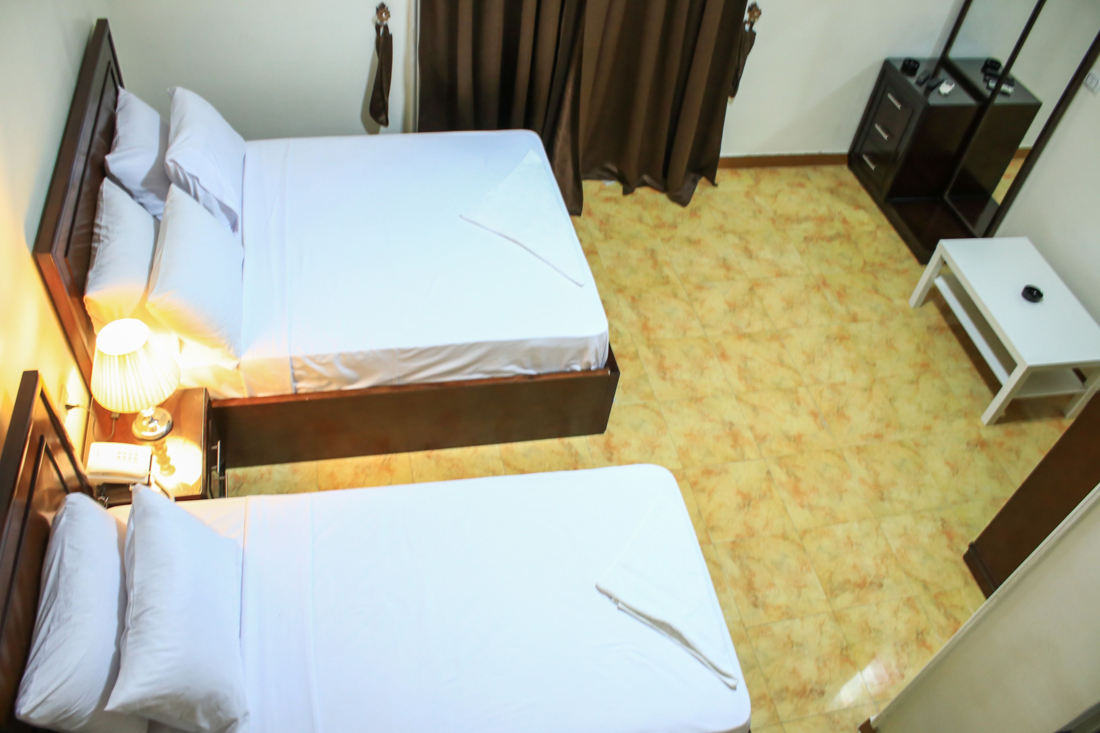 Ein Hotelzimmer mit zwei Betten, einem Nachttisch mit Lampe, einem kleinen Schreibtisch und einem Kleiderschrank.