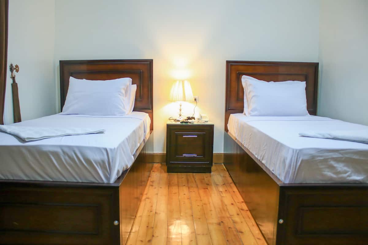 A hotel room with two single beds, a nightstand with a lamp, and a wooden floor.