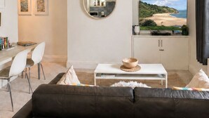 Una sala moderna con un sofá, una zona de comedor con sillas, un televisor y un ventanal con vista a la playa.