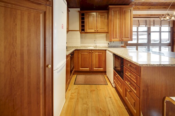 A kitchen with wooden cabinets, a granite countertop, and a wooden floor.