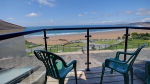 A balcony with two green plastic chairs overlooking a beach with a parking lot in the background. - 2 Bed in Clifton Court (oc-fl24) (Croyde)