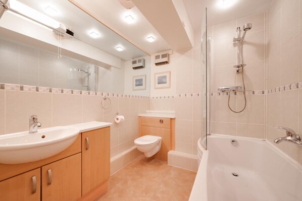 Un baño moderno con lavamanos, inodoro y bañera, con paredes y techo cubiertos de azulejos e iluminación empotrada.