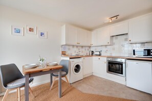 A modern kitchen with white cabinets, a washing machine, an oven, and a microwave.