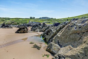 A coastal beach with large rocks, a sandy shore, and a building in the background.
