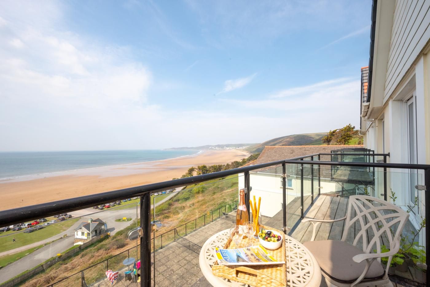 Un balcon avec vue sur la plage, une table garnie de nourriture et de boissons, et une chaise.