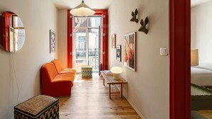 A hallway with a red sofa, a woven stool, and a table with a lamp. There are framed pictures on the walls and a mirror on the left. - ❤️The Traditional Arts Tribute | Sunny Balcony at Downtown! (Lisbon)