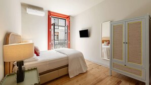 A bedroom with a bed, a bedside table with a lamp, a wardrobe, and a TV on the wall. - ❤️The Traditional Arts Tribute | Sunny Balcony at Downtown! (Lisbon)