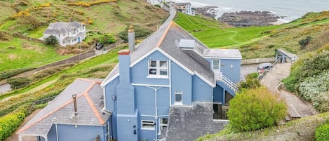 Una casa costera con techo inclinado, un camino de piedra y vista al mar.