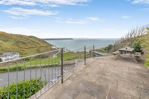 A stone staircase leading to a viewing platform with a metal railing, overlooking a coastal landscape with a body of water and a distant landmass.