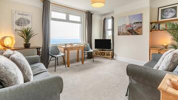 Un salon avec un canapé, un téléviseur, une table à manger et une vue sur la mer.