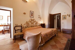 Een slaapkamer met een groot bed, een stoel, een nachtkastje en een kleine tafel.