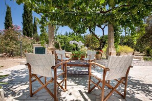A patio with four wooden chairs and a table, surrounded by greenery and trees. - 380 Villa Teresa by Perle di Puglia (Ugento)
