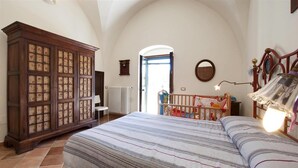 Un dormitorio con una cama grande, un armario de madera, un radiador, una cuna y una ventana con vistas.