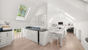 Eine moderne Küche mit weißen Schränken, ein Essbereich mit weißem Tisch und Stühlen sowie ein großes Dachfenster.