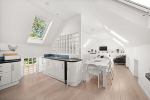 A modern kitchen with white cabinetry, a dining area with a white table and chairs, and a large skylight. - Historic 2‑Bedroom Central St Andrews Cottage Near West Port, Stylish Interiors & Walk to Old Course (St. Andrews)