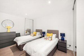A modern bedroom with two beds, a dresser, a mirror, and bedside lamps. - Historic 2‑Bedroom Central St Andrews Cottage Near West Port, Stylish Interiors & Walk to Old Course (St. Andrews)