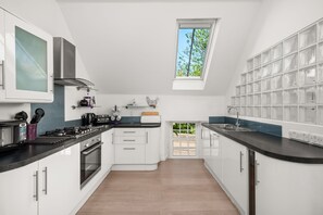 A modern kitchen with white cabinets, a black countertop, a skylight, and a view of greenery outside. - Historic 2‑Bedroom Central St Andrews Cottage Near West Port, Stylish Interiors & Walk to Old Course (St. Andrews)