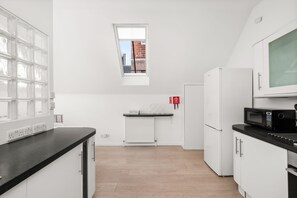 A modern kitchen with white cabinetry, a black countertop, a built-in microwave, and a window with a view of buildings.