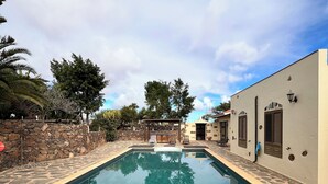 A rectangular swimming pool with stone-lined edges, surrounded by a stone wall and trees.