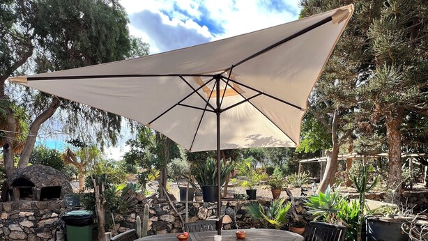 A stone-tiled patio with a round table and chairs, a large umbrella, and various potted plants.