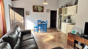 A living room with a black leather sofa, a dining area with blue chairs, a kitchen with a microwave, and a ceiling fan.