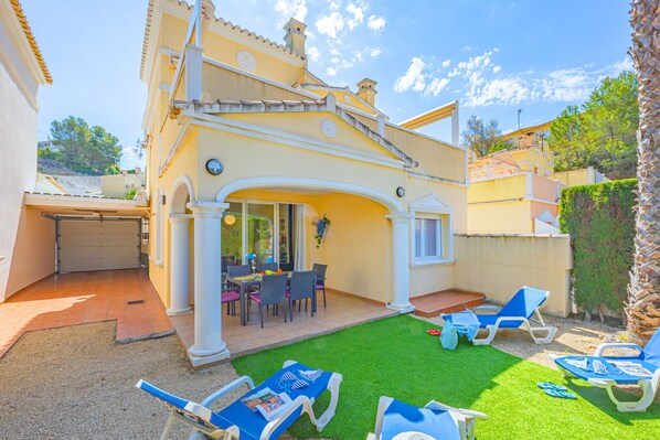 A yellow villa with a patio, outdoor seating, and a small garden.