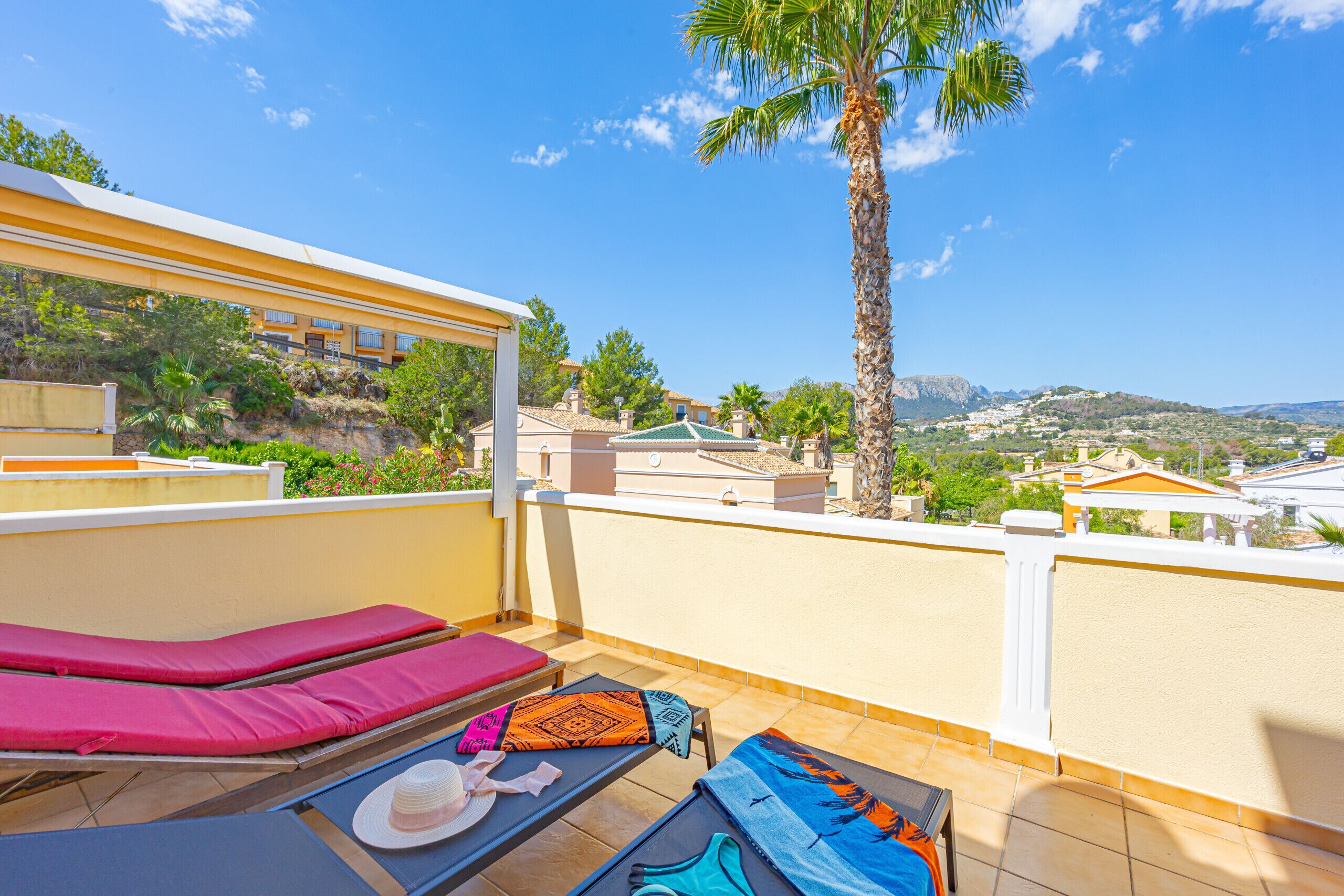 Un balcón con sillones de sol, una palmera y vista a un pueblo costero.